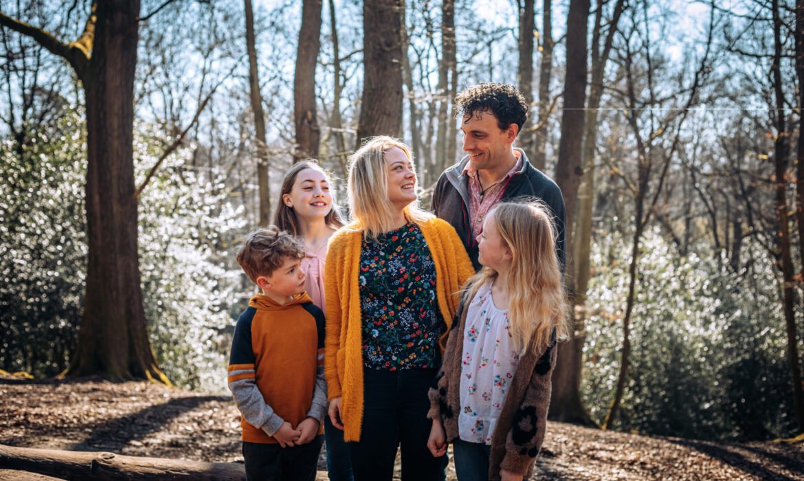 A family of five, surrounding and looking at mum in the woods in Autumn.