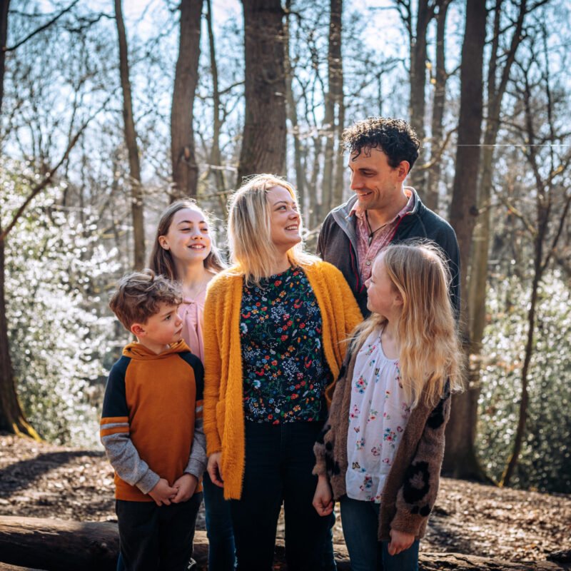 A family of five, surrounding and looking at mum in the woods in Autumn.