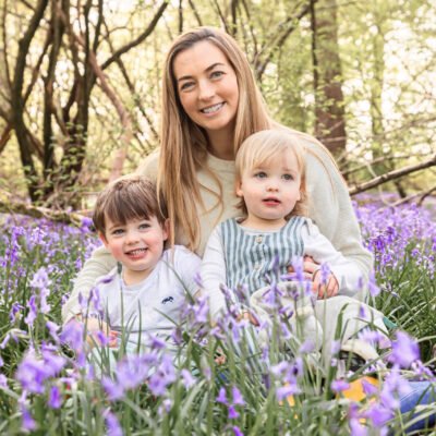 A mum sitting in the bluebells with her two children.