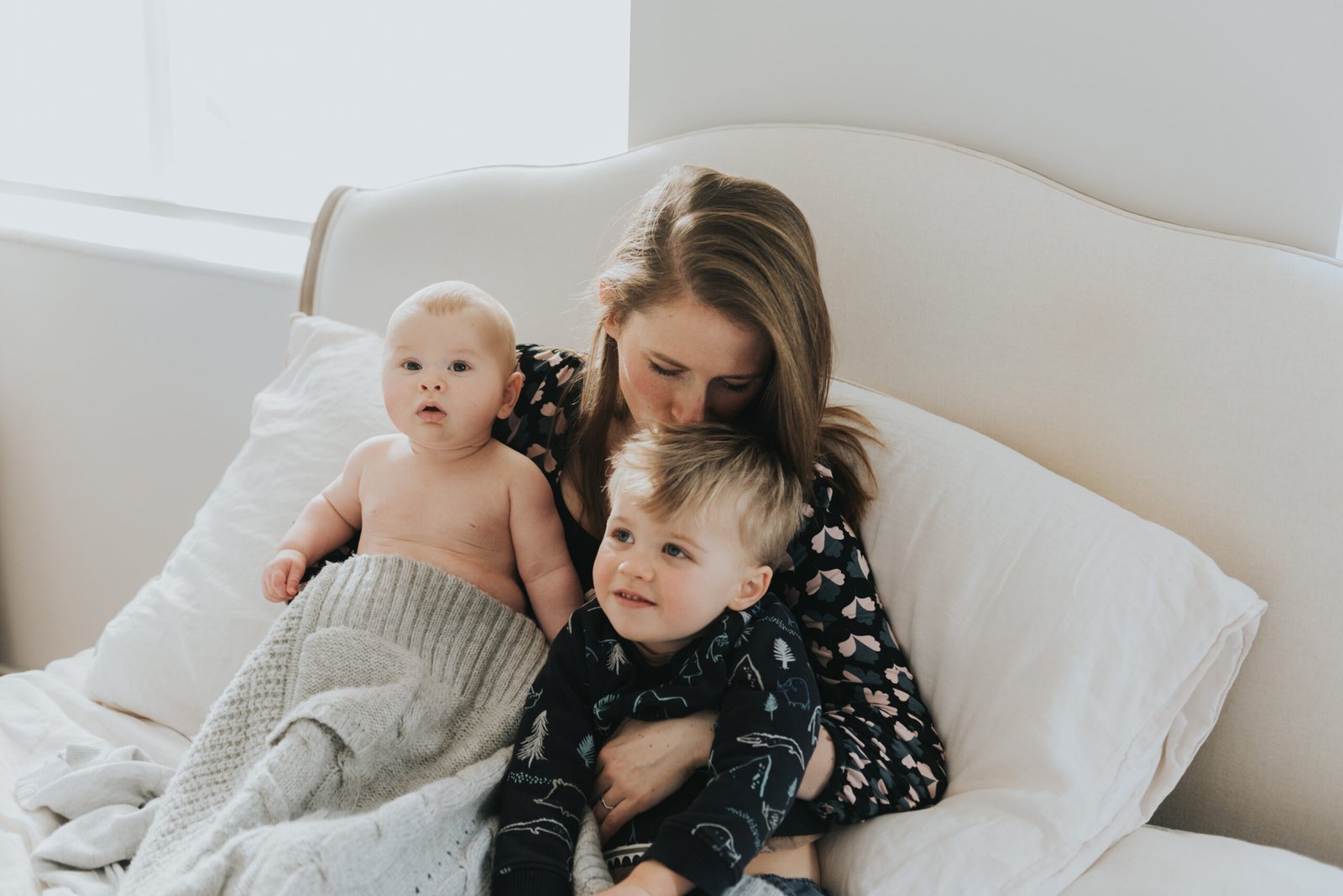 Mum and her two sons sitting in bed with mum kissing her eldest son on the head