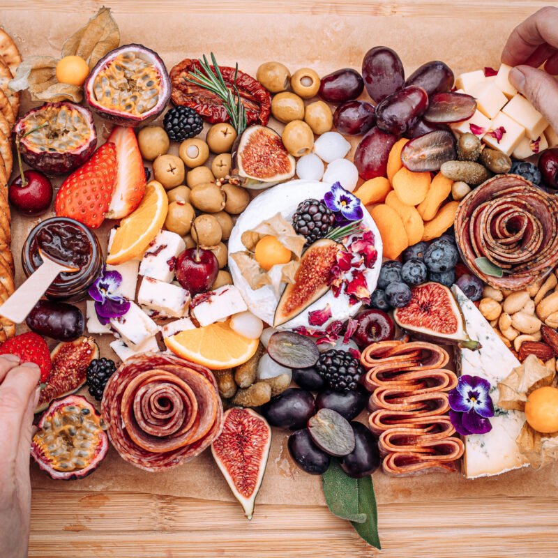 Branding photography of a grazing board from above, rich colours showing hands arranging the food on a wooden board.