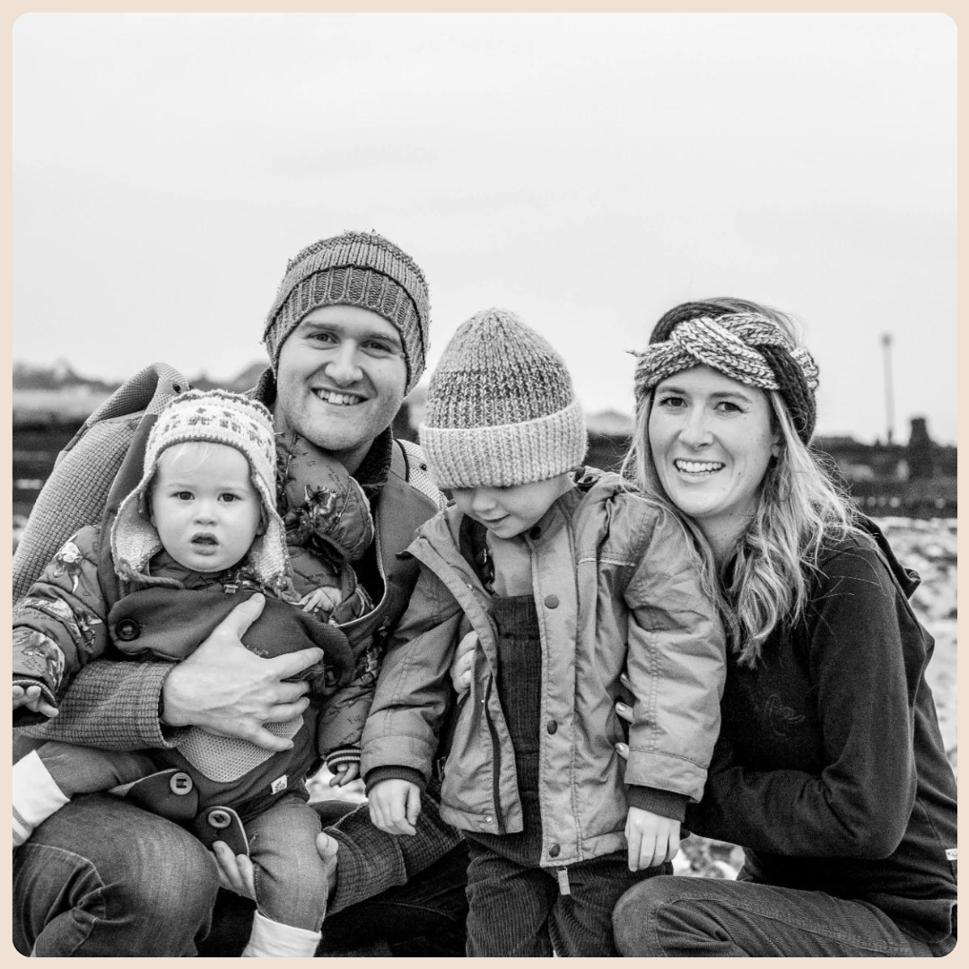 A black and white family portrait of four on a winter beach in West Sussex, wearing wooly hats.