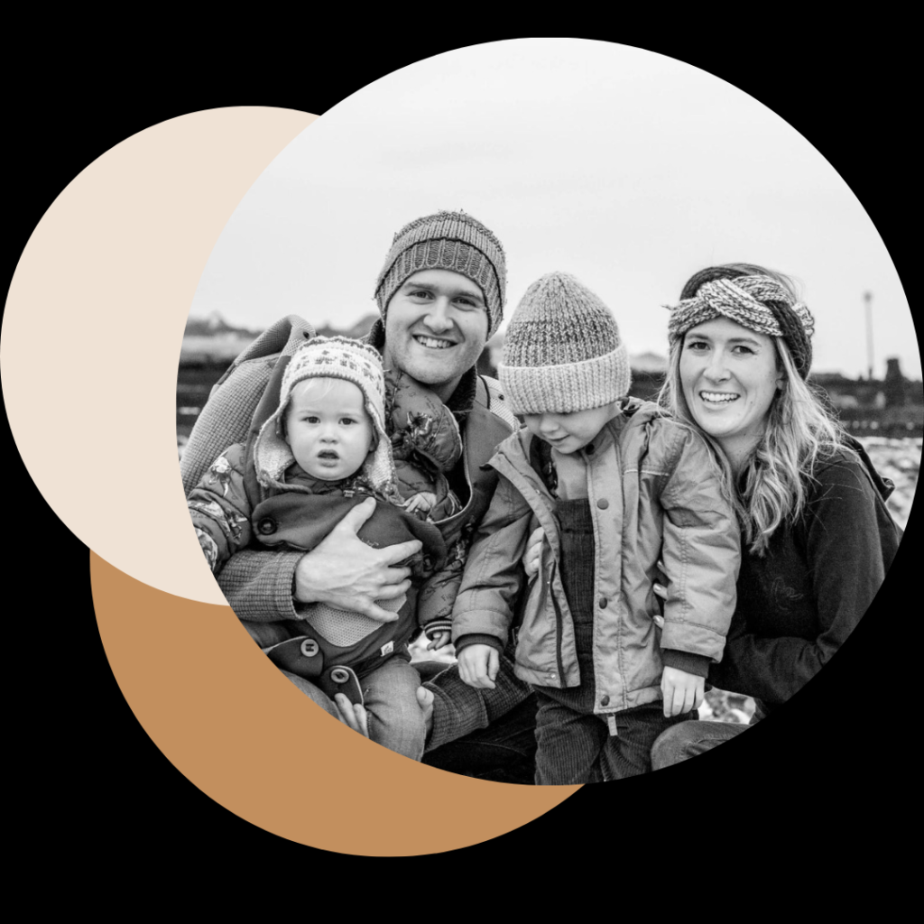 A black and white family portrait of four on a winter beach in West Sussex, wearing wooly hats.