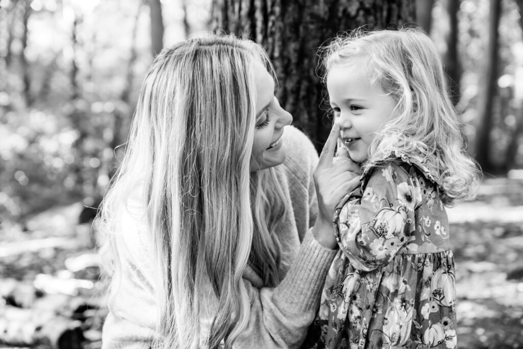 Mum and young daughter in the woods, mum with her finger on the girls nose, looking at each other.