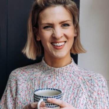 Personal branding portrait of a lady smiling at the camera, in a chunky knit, with a cup of tea